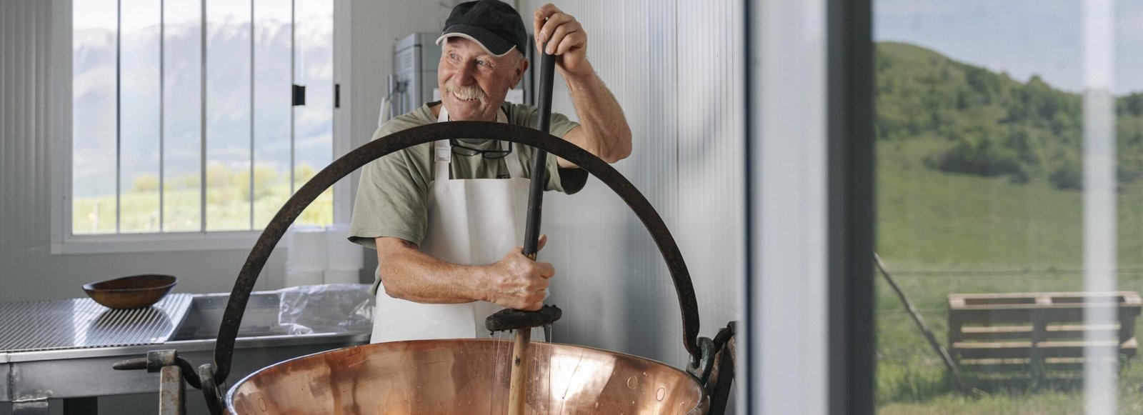 Casaro mescola latte nel calderone con vista sulle montagne