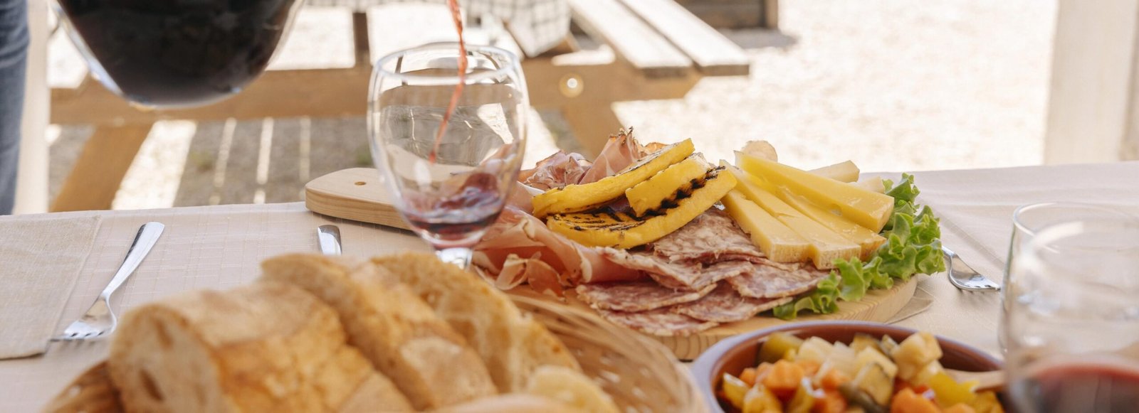 Tagliere con salumi, formaggi e vino rosso su tavolo all’aperto